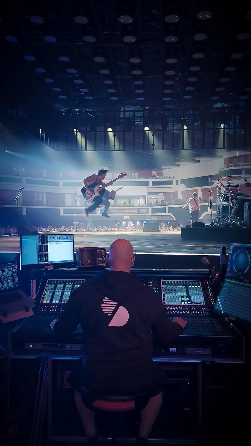 Mike Osman mixing at a DiGiCo console, seen from behind, as a bass player leaps on stage in a lit arena